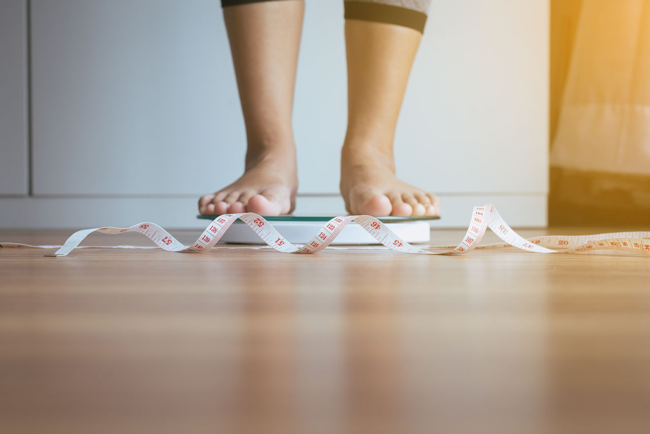 Woman feet standing on weigh scales with tape measure in foreground,Weight loss,Body and healthcare concept,Woman feet standing on weigh scales with tape measure in foregro