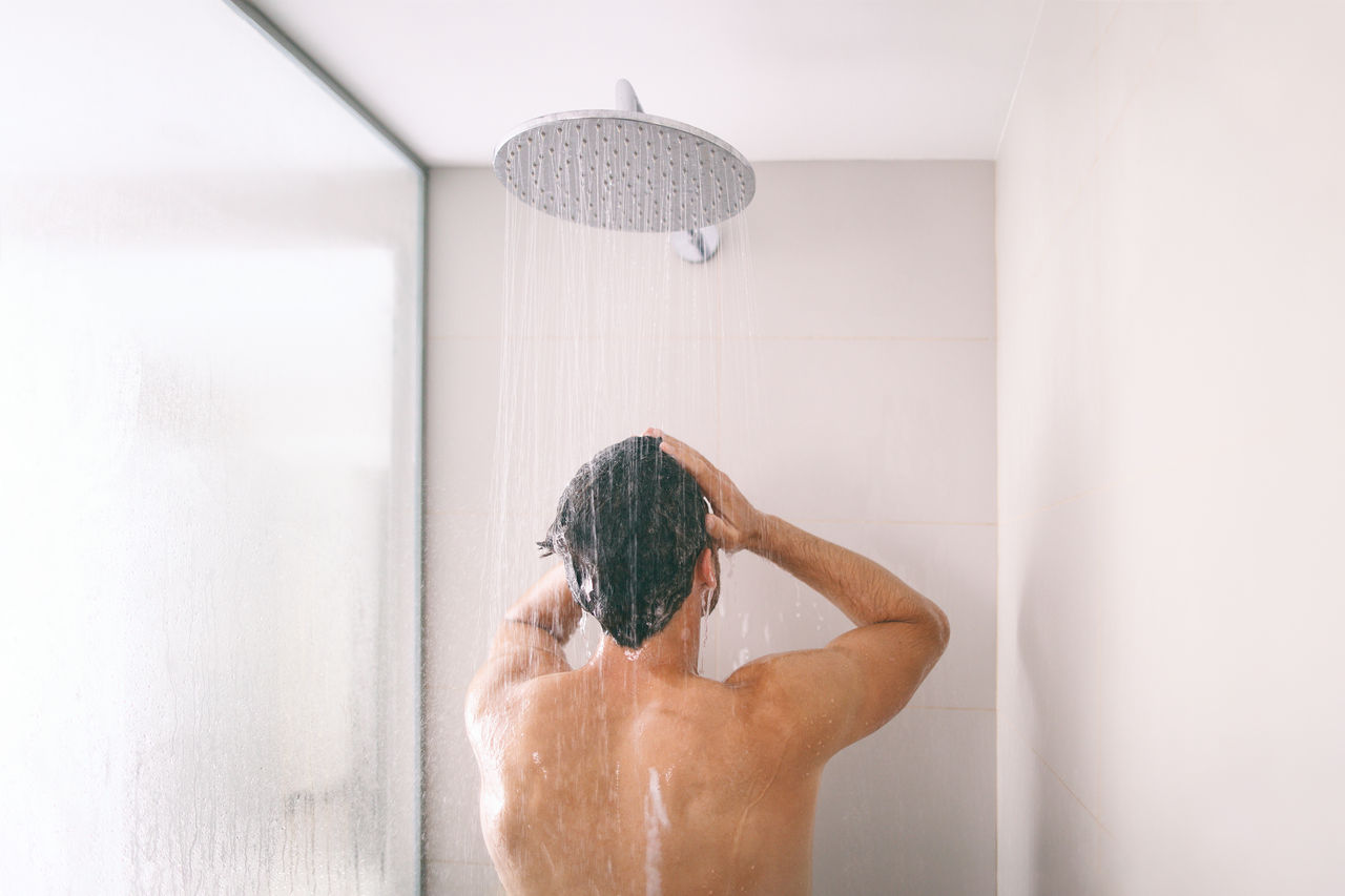 Man taking a shower washing hair with shampoo product under water falling from luxury rain shower head. Morning routine luxury hotel lifestyle guy showering. body care hygiene.,Man taking a shower washing hair with shampoo product under wate
