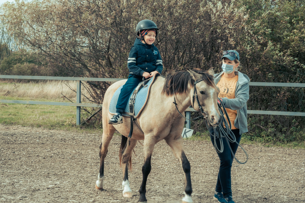 A child with special needs is riding with a close supervision teacher. This is a treatment called Hippotherapy, Life in the education age of disabled children, Happy disability kid concept. quarantine,A child with special needs is riding with a close supervision te