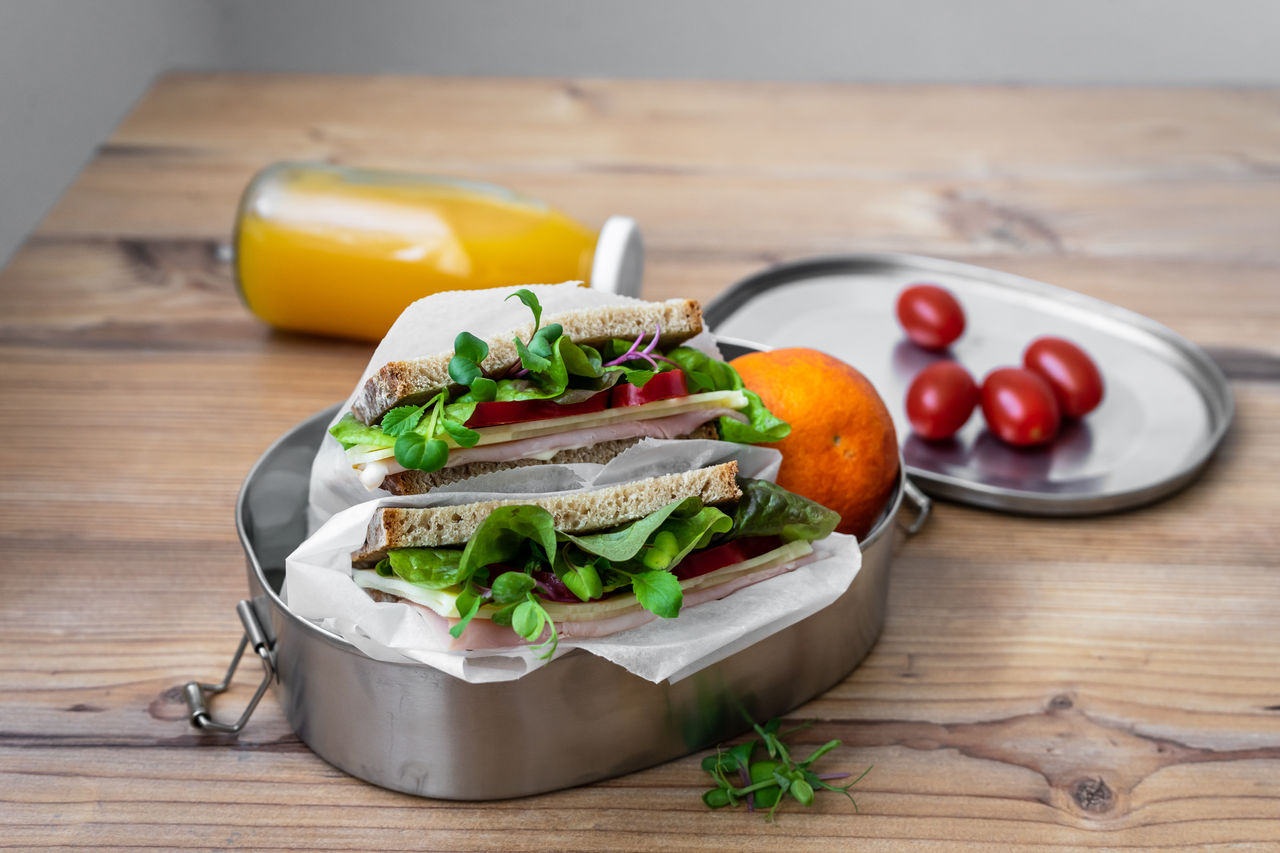 Sandwich mit Salatblätter und Schinken in einer wiederverwendbaren Blechdose, Orangensaft und Cocktailtomaten auf einem Holz Tisch.,Sandwich mit Salatblätter und Schinken in einer wiederverwendba