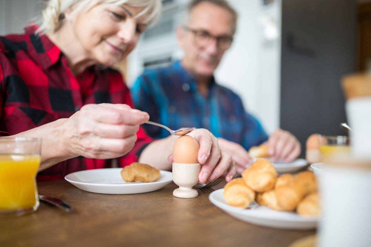 Senior woman breaking boiled egg for breakfast