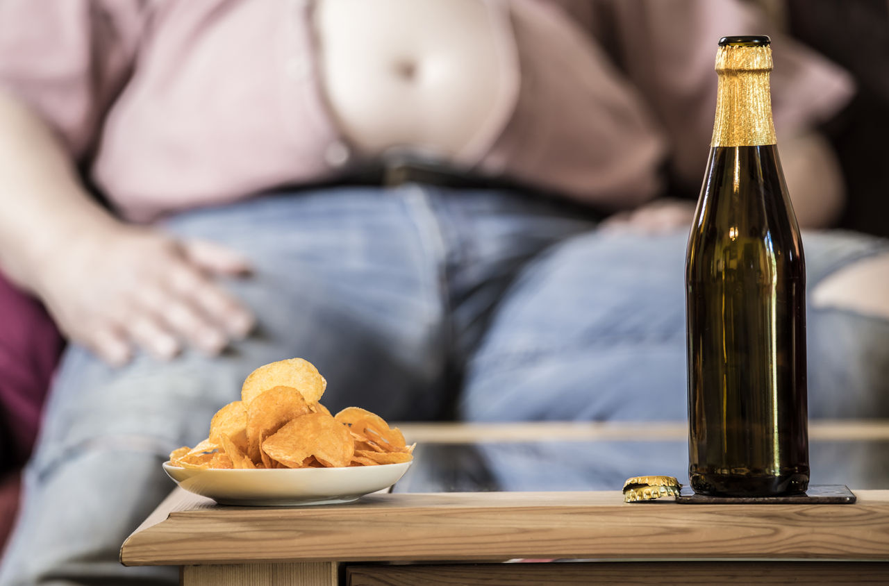 ein dicker Mann sitzt an einem Tisch auf dem Bier und Kartoffelchips stehen,ein dicker Mann sitzt an einem Tisch auf dem Bier und Kartoffelc