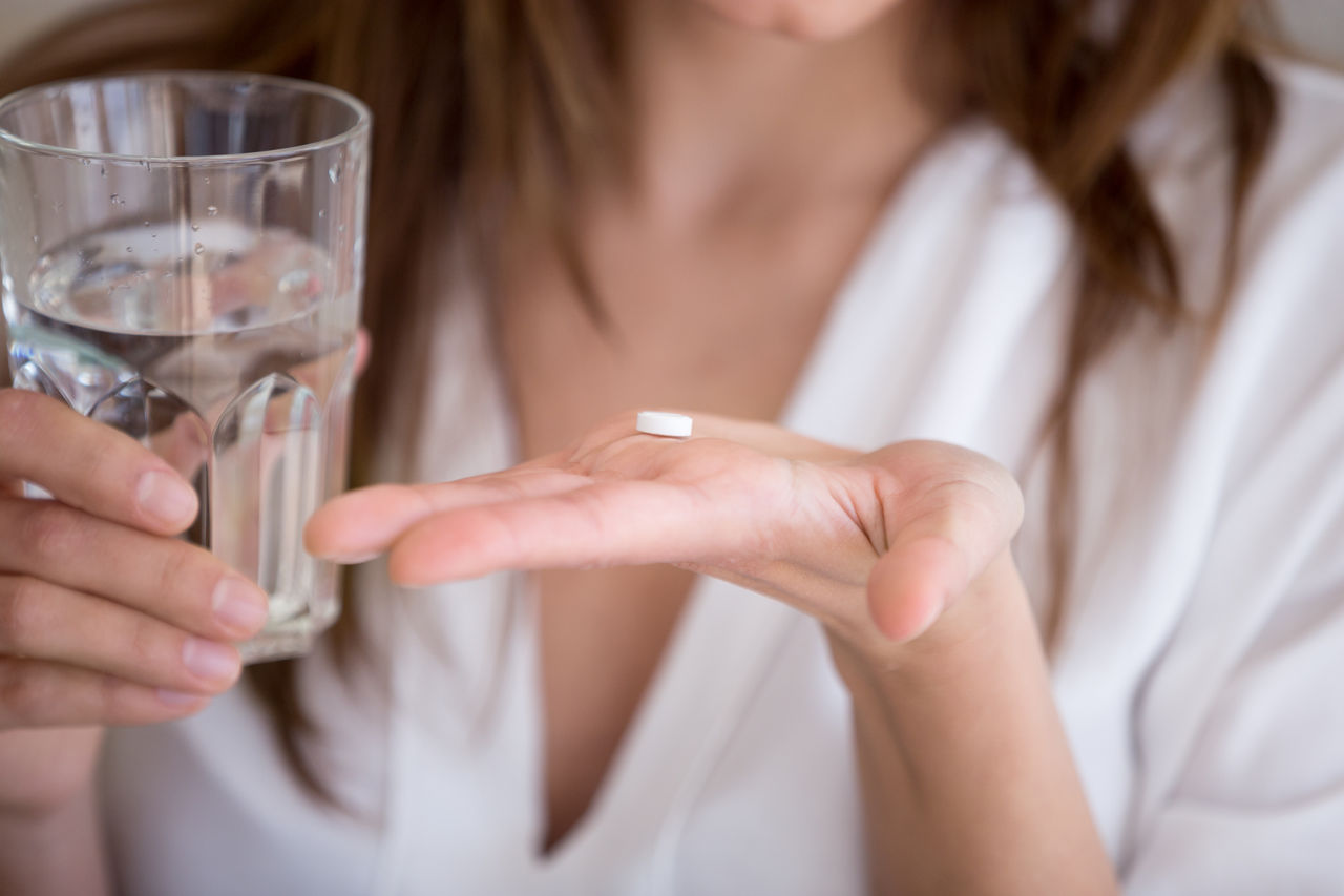 Woman holding pill and glass of water, close up view