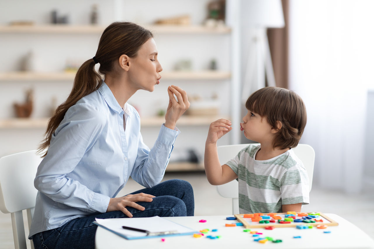 Young woman speech therapist studying together with small kid, learning practice pronunciation exercises with little boy,Young woman speech therapist studying together with small kid, l