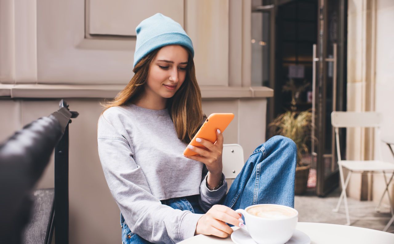 Young millennial female using social network application on mobile phone for communication. Caucasian hipster girl holding smartphone in silicone case. Teenager browsing online with internet data,Young millennial female using social network application on mobi