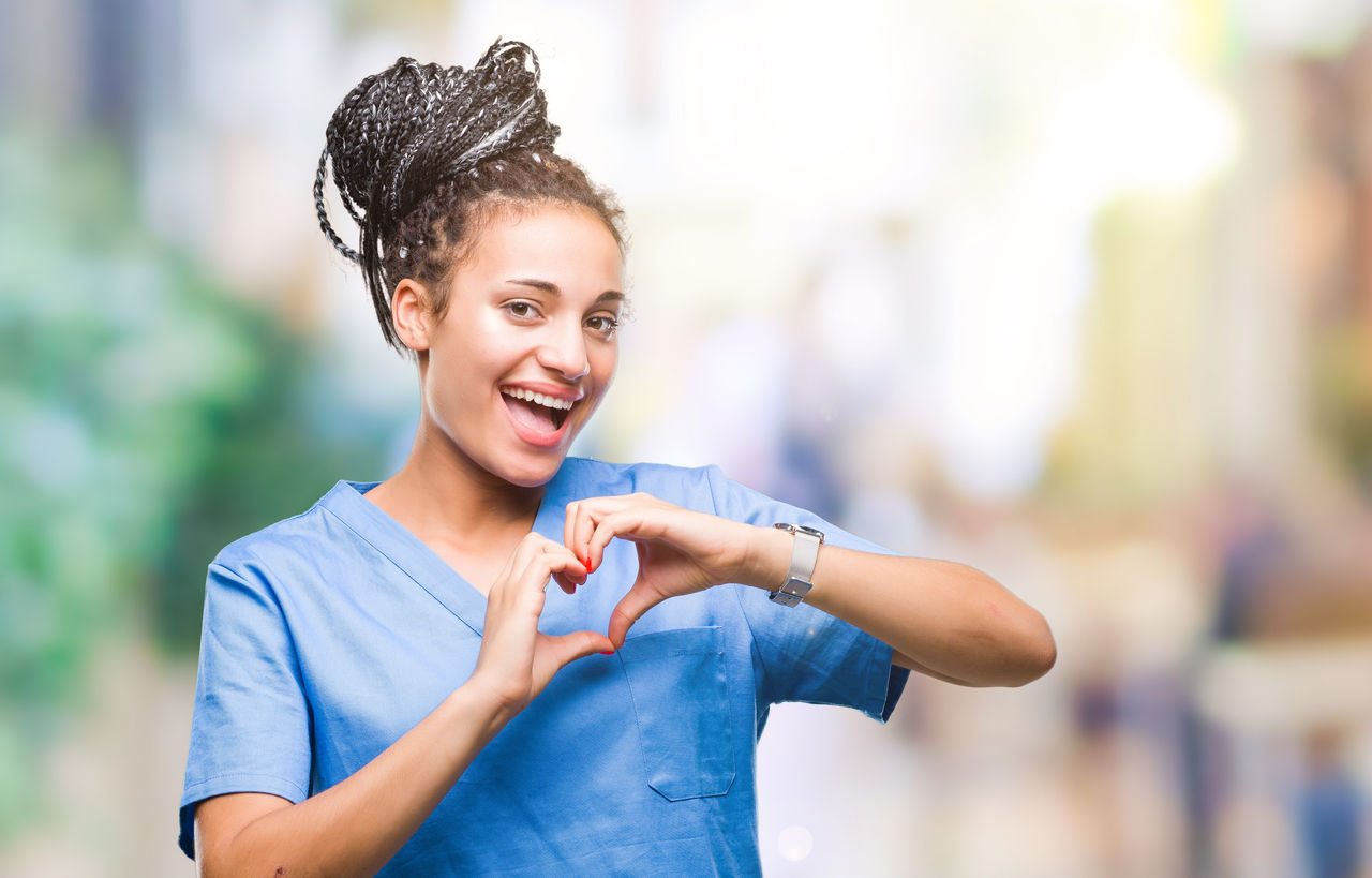 Young braided hair african american girl professional nurse over isolated background smiling in love showing heart symbol and shape with hands. Romantic concept.,Young braided hair african american girl professional nurse over