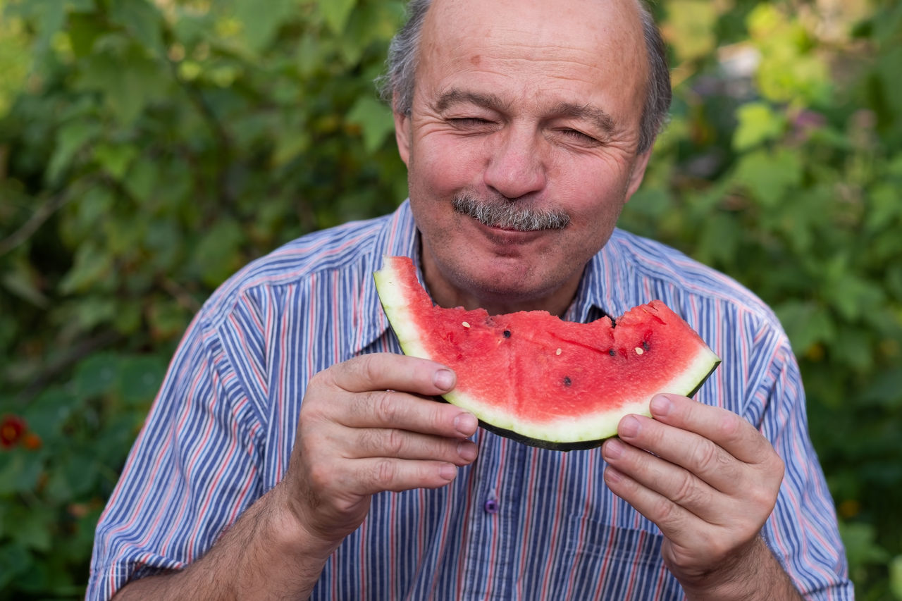 Mature caucasian man with mustache eating juicy water melon with pleasure and smiling.,Mature caucasian man with mustache eating juicy water melon with