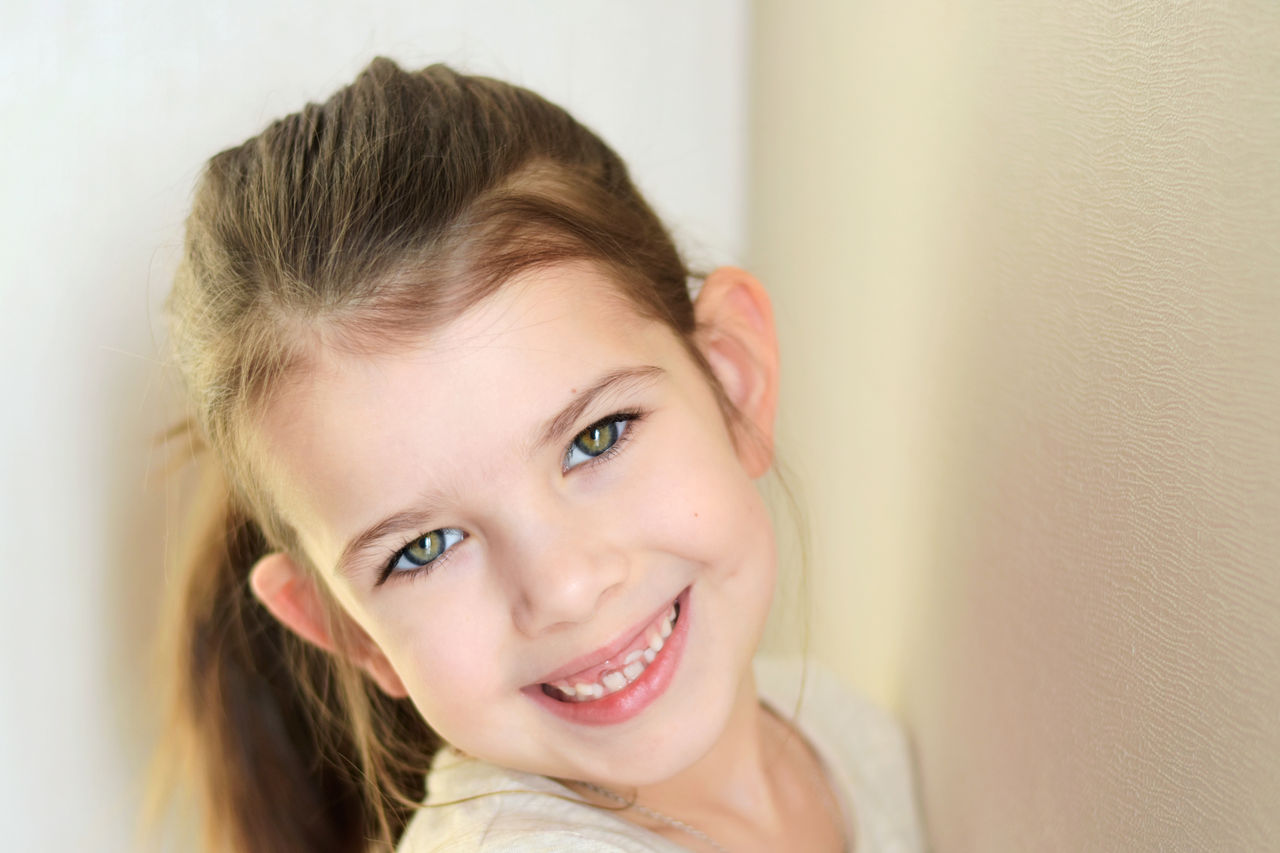 portrait of a little caucasian white beautiful brunette girl with pony tail on neutral background. smiling toothless green eyed happy girl with cute protruding ears. Kid expression portrait with fun h,portrait of a little caucasian white beautiful brunette girl wit