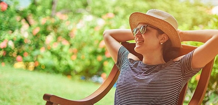 Frau mit Sonnenhut und Sonnenbrille auf Gartenstuhl