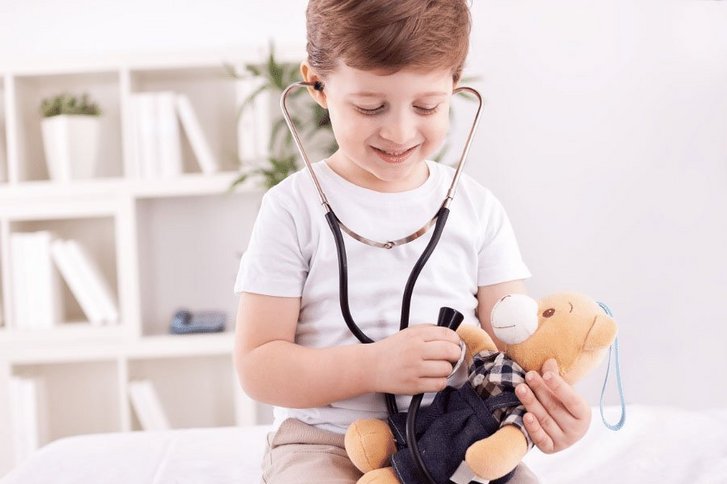 Ein Junge trägt ein Stetoskop um den Hals und verarztet einen Teddy. 