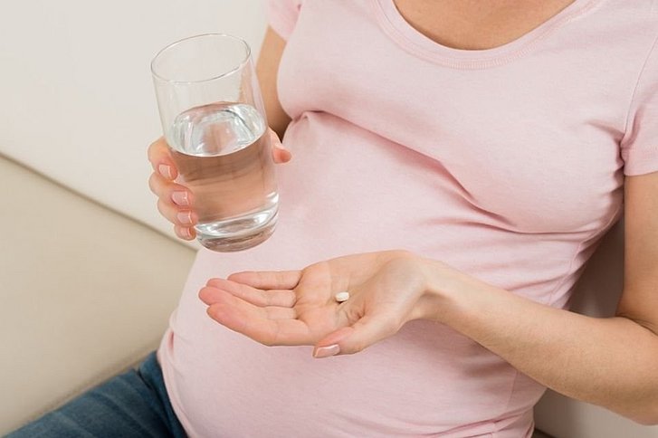 Schwangere mit Glas Wasser und Tablette