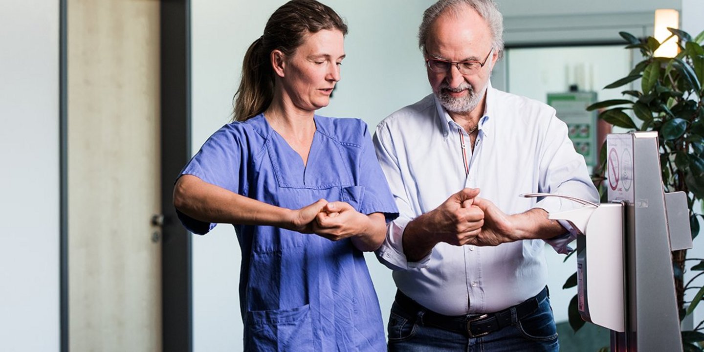 Foto einer Pflegekraft, die einem Patienten die Händedesinfektion zeigt