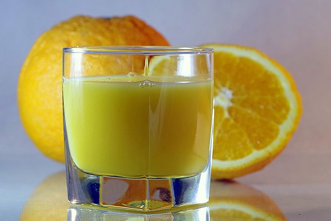 Ein Glas mit Orangensaft befüllt. Im Hintergrund Orangenscheiben. 