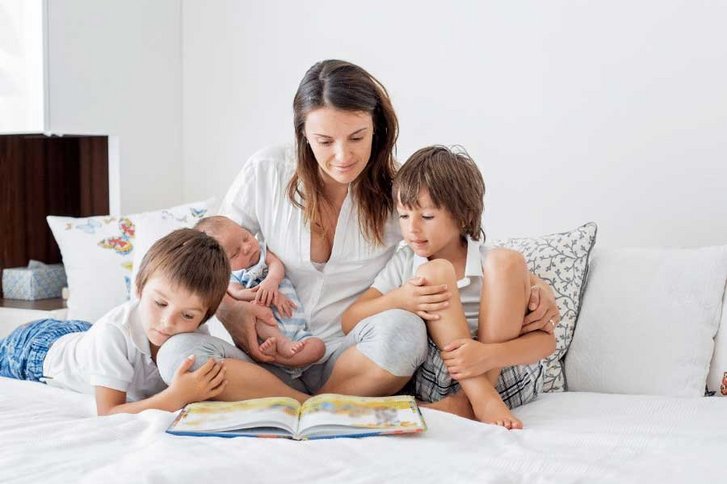 Mutter ließt ihren drei kleinen Kindern ein Buch im Bett vor. 