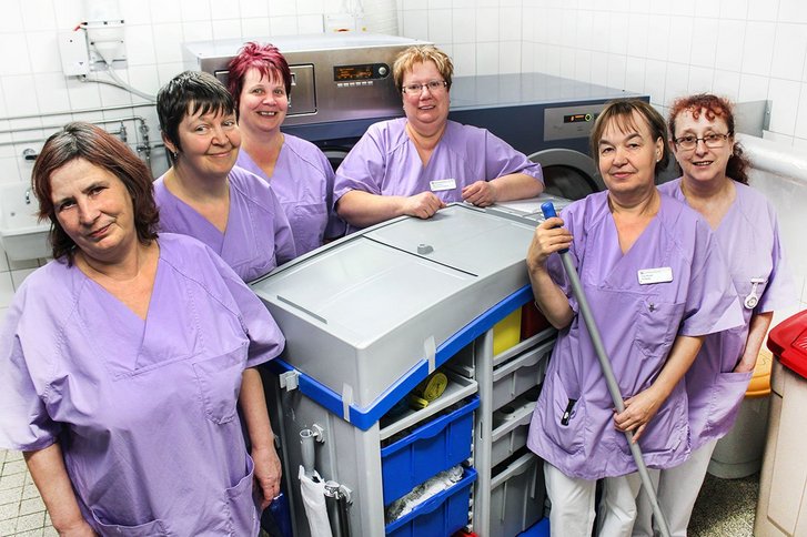 Sechs Frauen in violetten Kassacks stehen um einen Reinigungswagen