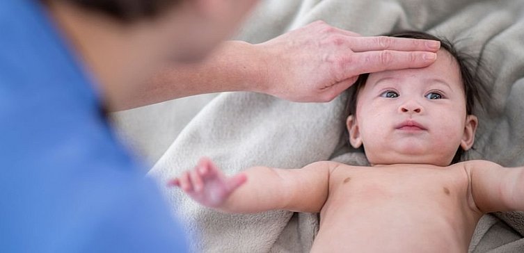 Frau legt Finger auf Stirn von Baby