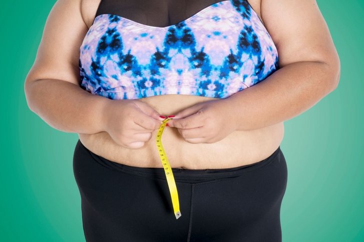 Übergewichtige Frau misst ihren Bauchumfang mit Maßband