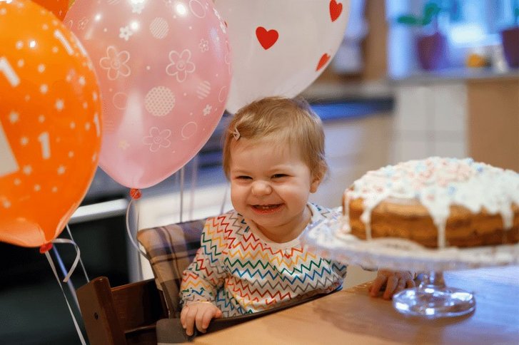 Kleines Mädchen sitzt an einem Tisch mit einer Geburtstagstorte. 