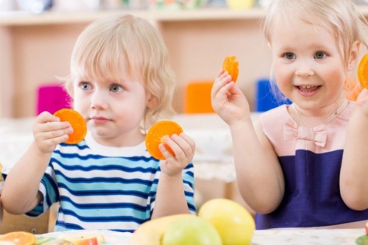 Kinder am Esstisch, sie essen Obst und Gemüse. 