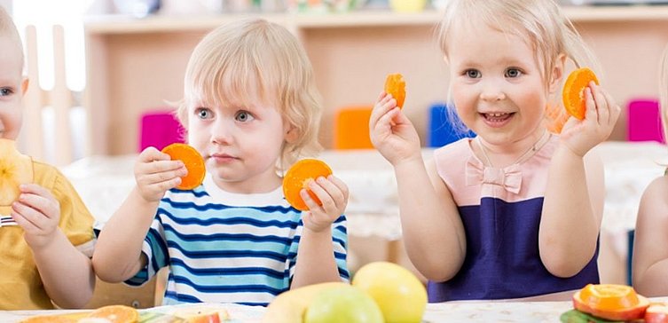 Kinder am Esstisch, sie essen Obst und Gemüse. 