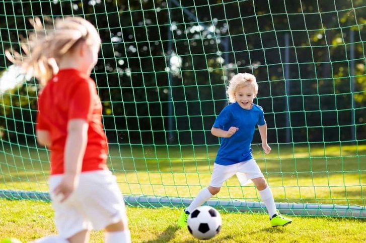 Junge und Mädchen spielen Fußball. Mädchen schießt aufs Tor. 