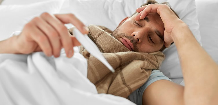 Ein Mann liegt mit einem grippalen Infekt im Bett