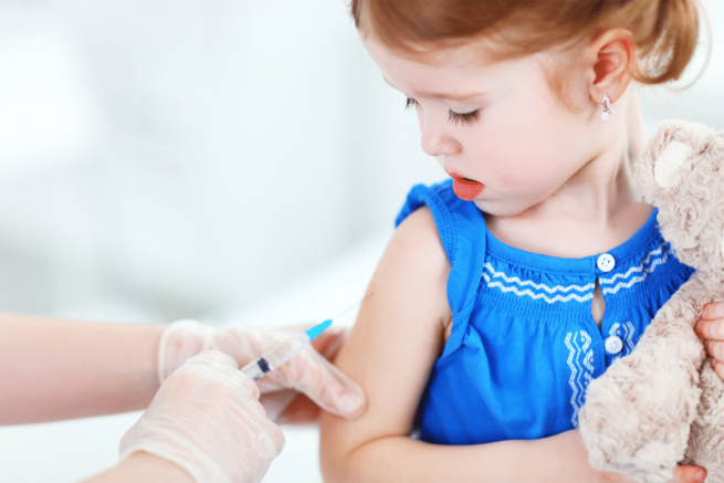 Ein kleines Mädchen wird geimpft, es schaut ängstlich auf ihren Arm und die Spritze