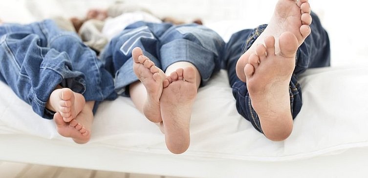 Frau, Mann und Kind liegen mit nackten Füßen im Bett | Helios Gesundheit