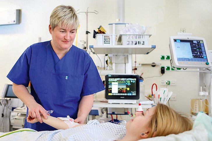 Krankenpflegerin hält den Arm einer jungen im Bett liegenden Frau