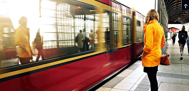 Frau in gelben Mantel warten auf einfahrenden S-Bahn