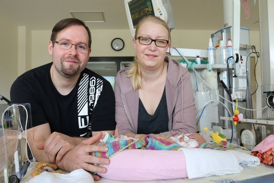 Ein Mann und eine Frau stehen vor Krankenbett in dem Fruechen liegt
