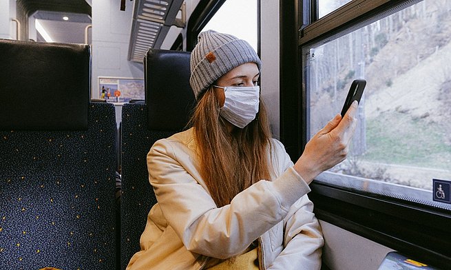 Frau mit Handy und Mund-Nasen-Schutz in der Bahn