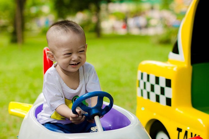 asiatischer Junge im Laufrad hat eine Hand fest am Steuer und freut sich stark durch den Park zu fahren