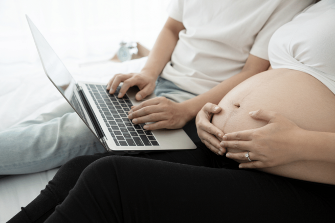 Schwangeres Paar schaut in einen Laptop auf dem Schoß der Frau