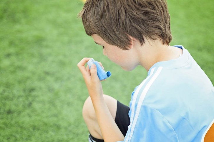  Ein Junge mit blauem Shirt benutzt einen Inhalator.