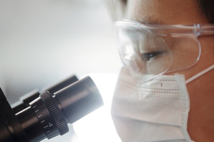 Mann mit Mund- und Sichtschutz blickt in Mikroskop