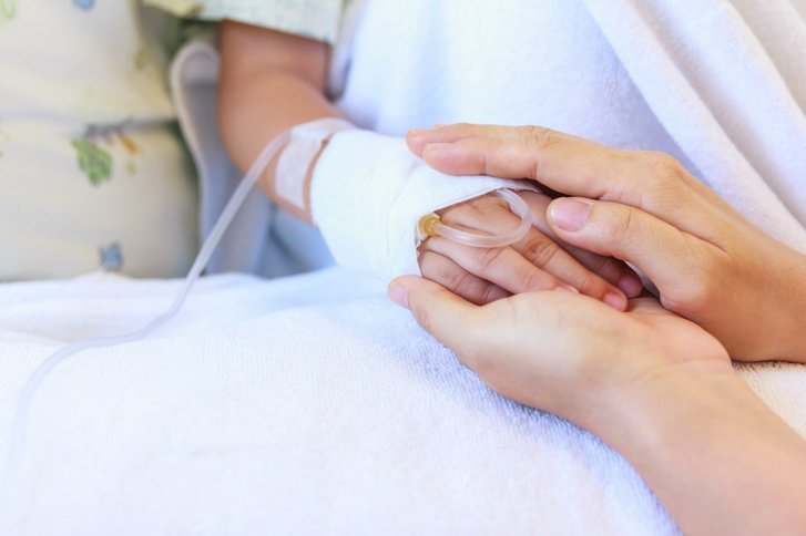 Erwachsenenhand umschließt Hand eines Kindes im Krankenbett