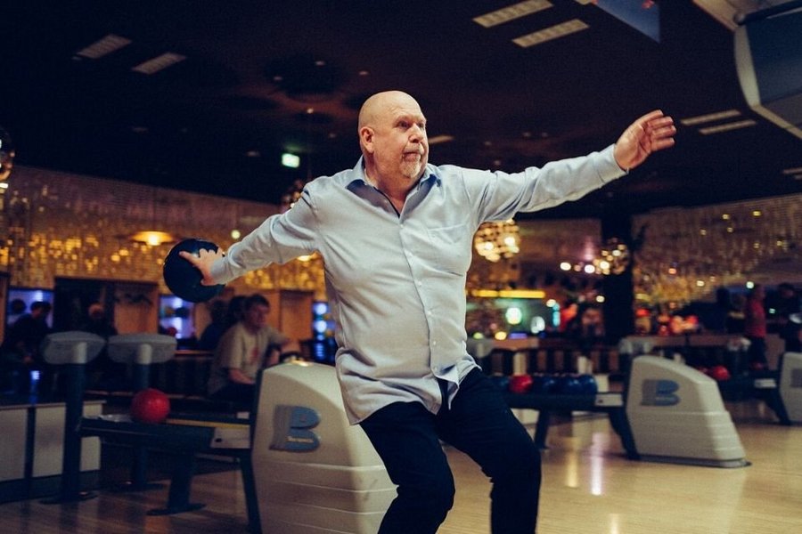 Mann im Bowlingcenter wirft Bowlingkugel auf Bowlingbahn