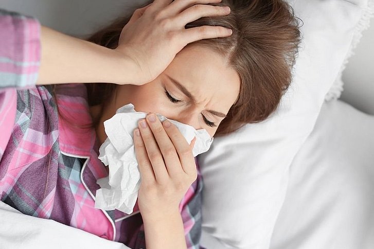 Frau mit Taschentuch an Nase im Bett