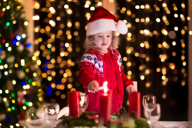 kleines Mädchen mit Weihnachtsmütze zündet Kerzen an