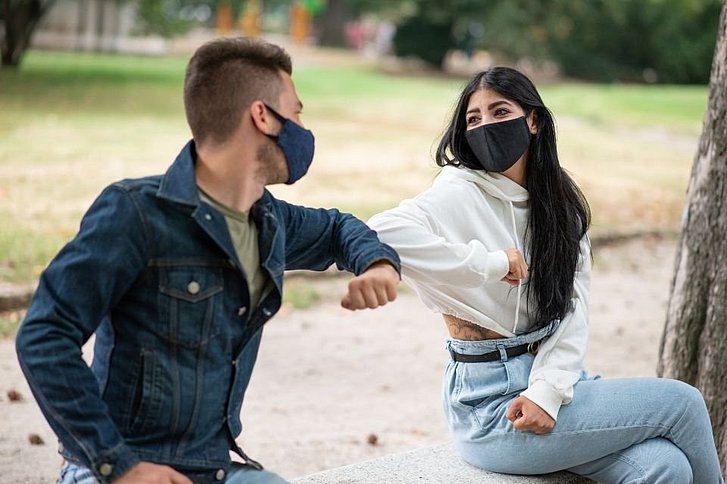Junge und Mädchen tragen Stoffmasken und sitzen auf Bank