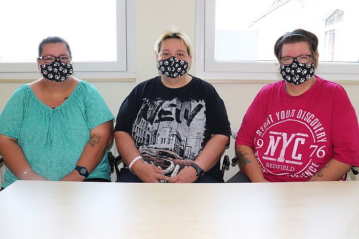 Drei Frauen mit Mund-Nasen-Schutz sitzen am Tisch