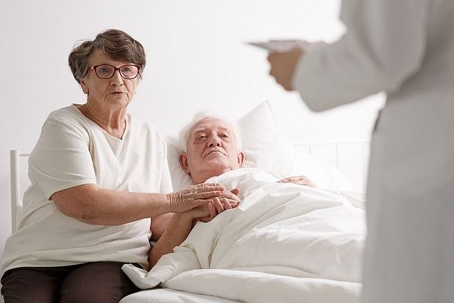 Ältere Frau am Bett ihres Mannes im Krankenhaus