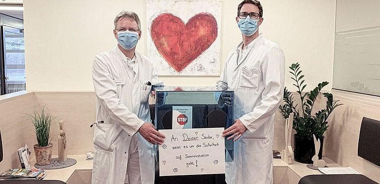 Zwei Männer in Arztlkittel halten ein Schild