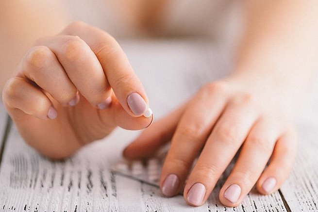 Frauenhand hält Antibabybille in den Fingern