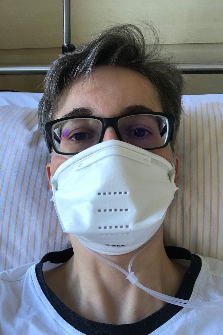 Frau mit Atemschutzmaske und Brille liegt im Krankenhausbett