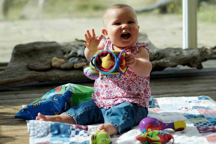 Korpulentes Baby sitzt auf einer Picknickdecke und spielt 