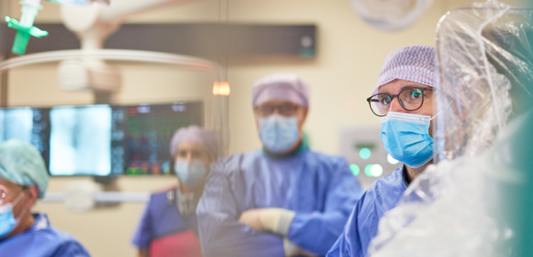 Mehrere Menschen stehen mit OP-Kleidung in einem Operationssaal.
