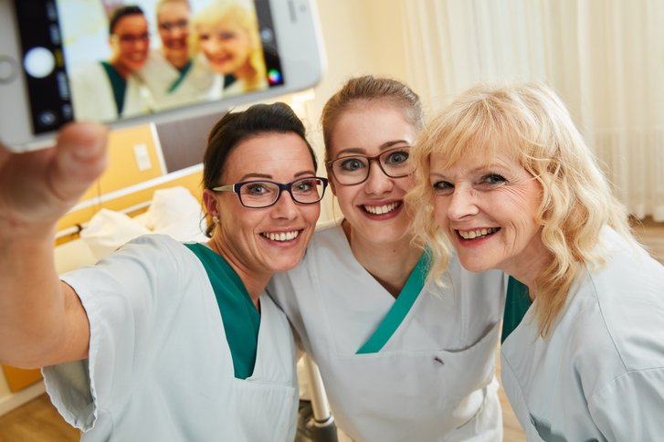 Selfie von drei Pflegekräften in einem leeren Patientenzimmer