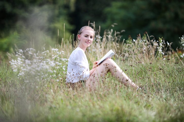 Junge Frau sitzt mit Buch in Gras